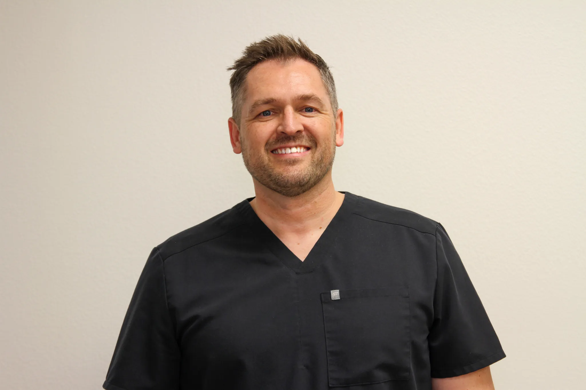 Dr. Travis Hailstone DO wearing grey clinical scrubs and a stethoscope inside the family practice clinic.
