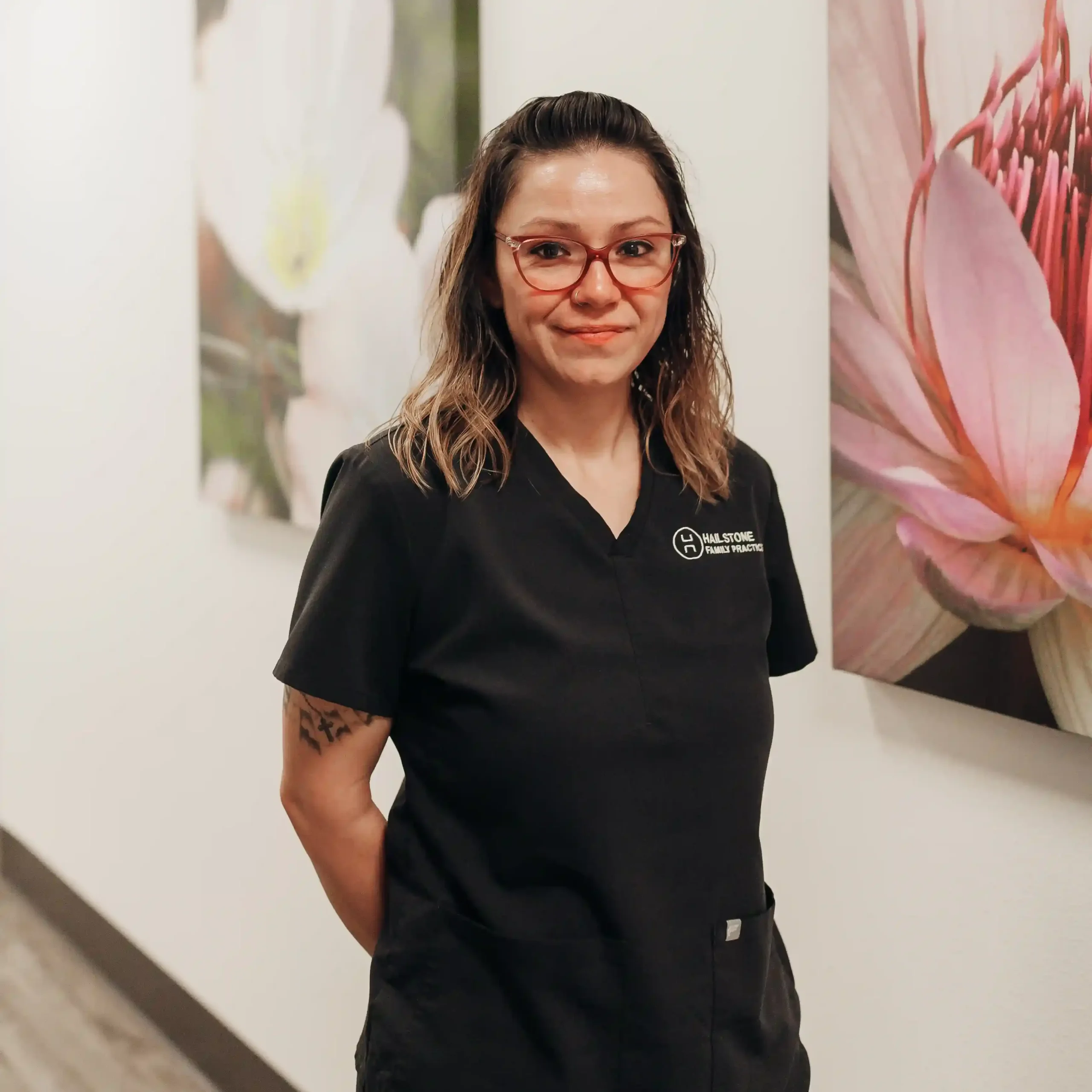 Practice team member Krystal Cuna wearing red glasses and black scrubs standing before a pink lotus canvas frame.