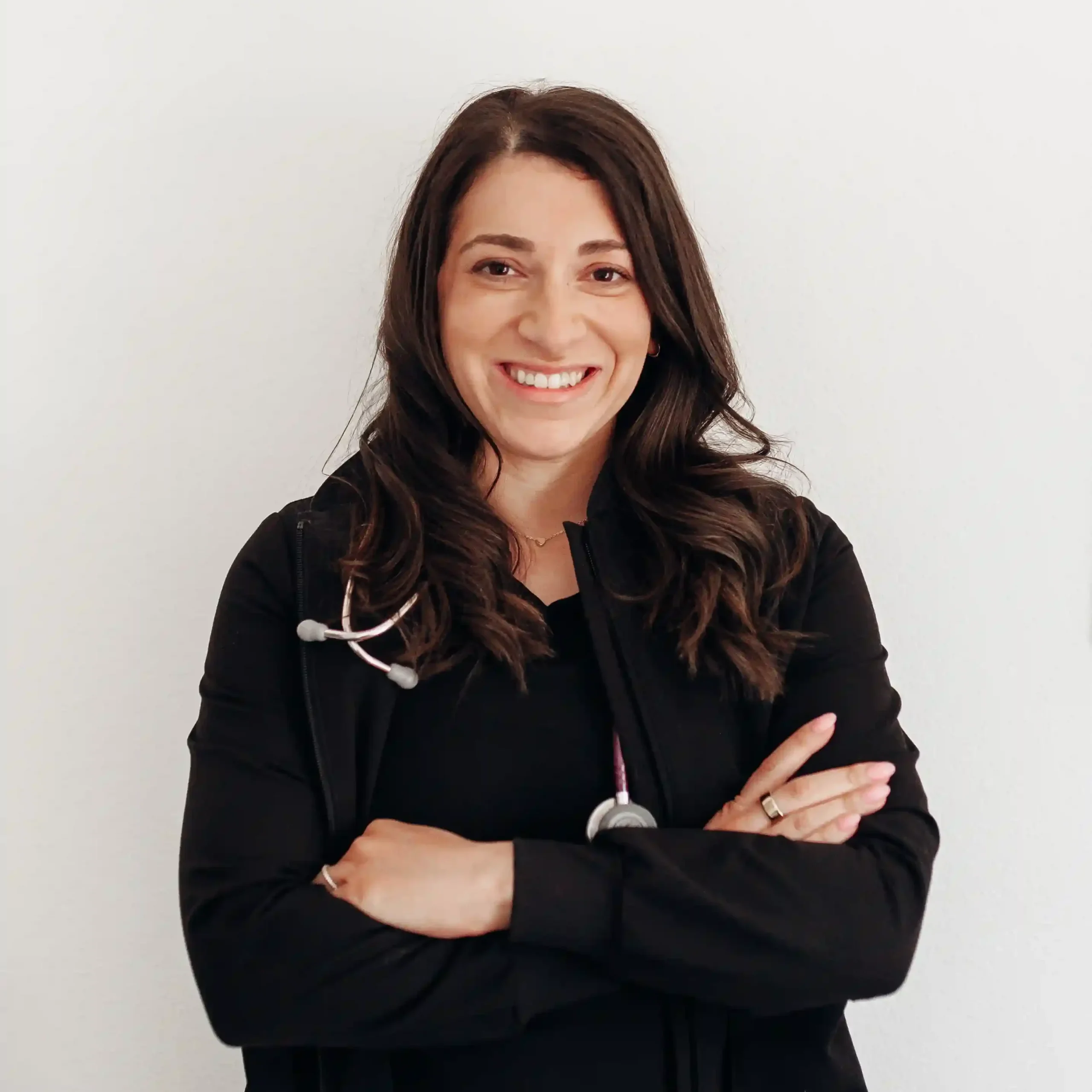 Family nurse practitioner Lauren Bedrock smiling with arms crossed against a white clinical office wall.