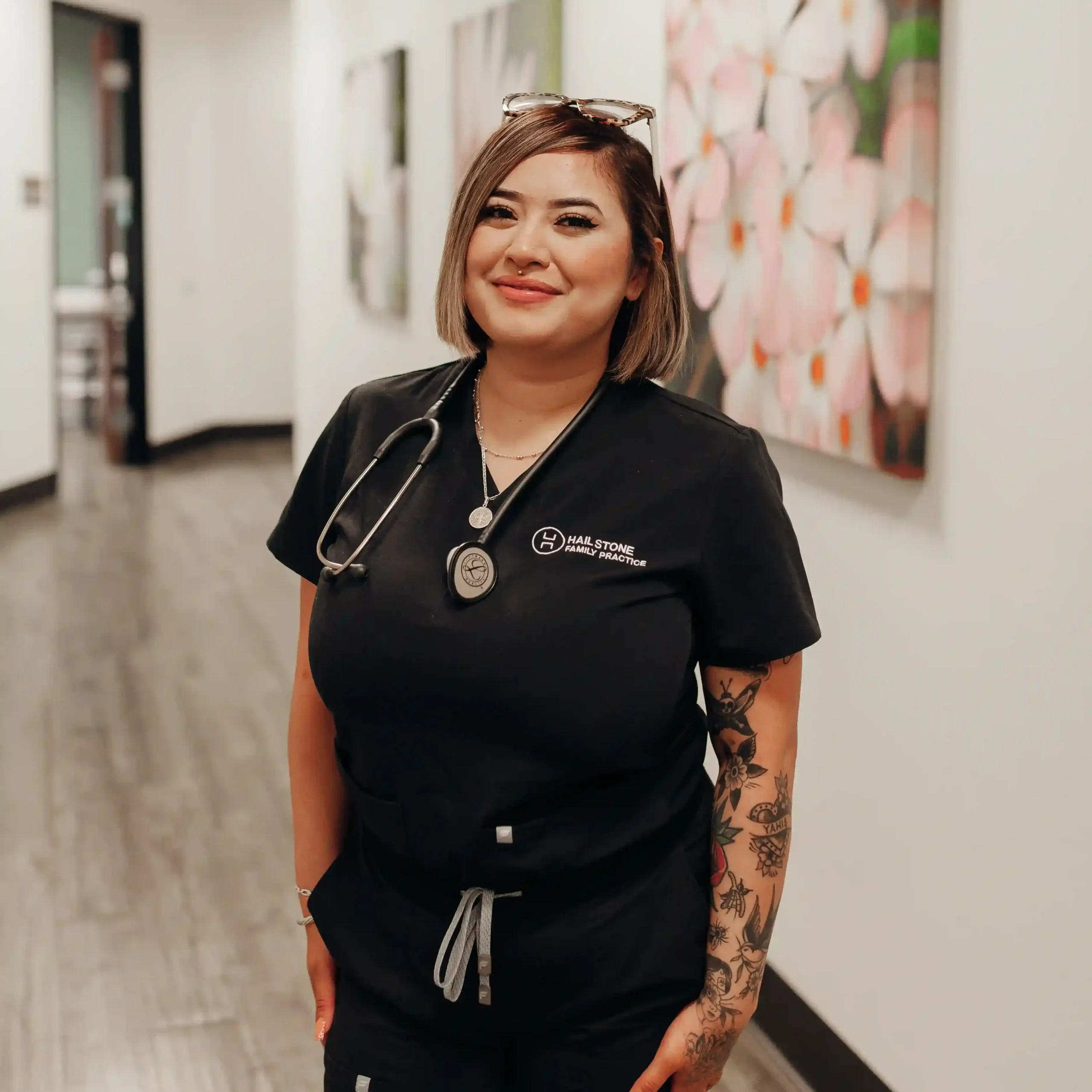 Medical professional Zeyla Bacerra wearing black scrubs and a stethoscope in a hallway with floral dahlia canvas art.